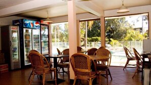 A restaurant with wicker chairs and tables, a Pepsi refrigerator, and large windows overlooking a pool.