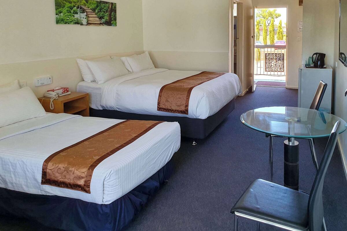 A hotel room with two beds, a glass table, a chair, a phone, and a painting on the wall.
