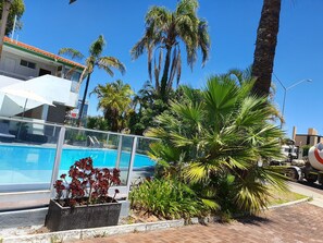 A swimming pool surrounded by palm trees and a concrete planter with red flowers.