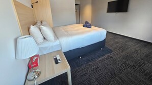 A hotel room with a bed, a bedside table with a lamp, a TV, and a wall-mounted air conditioner.