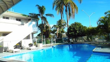 Una piscina con palmeras y un edificio al fondo.