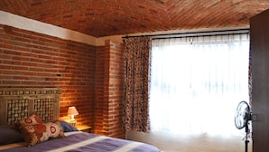 Une pièce avec un plafond en briques, un lit agrémenté d’oreillers à motifs, une table de chevet avec une lampe et une fenêtre avec des rideaux.