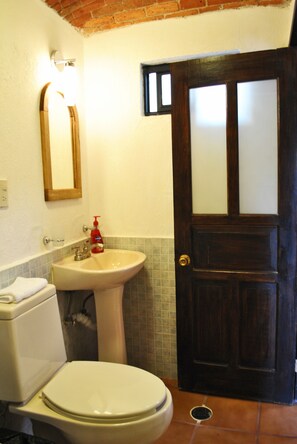 A bathroom with a toilet, sink, and a wooden door with frosted glass panels. - Casa Geranios Tequisquiapan (Tequisquiapan)