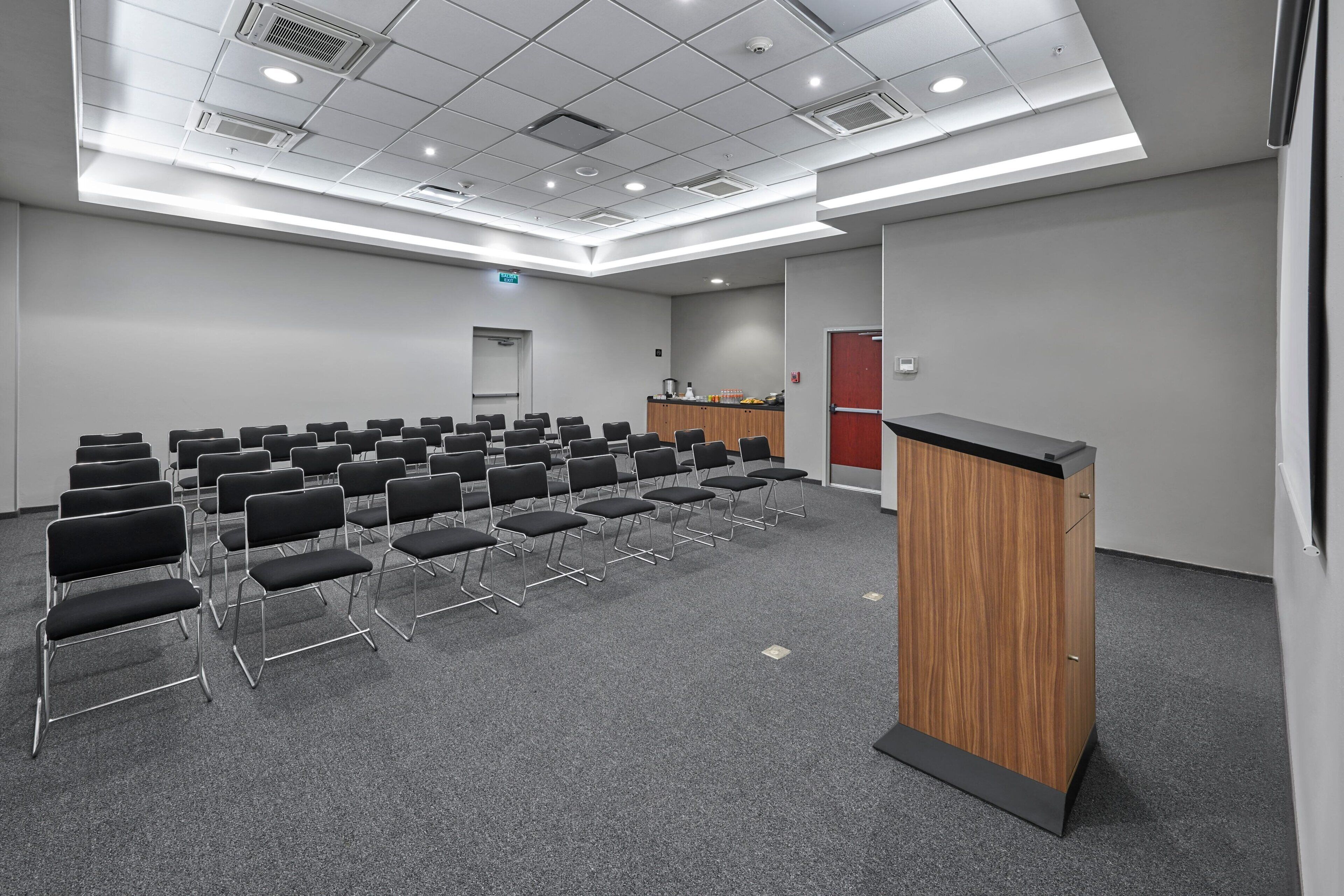 A conference room with rows of chairs, a podium, and a kitchenette area.