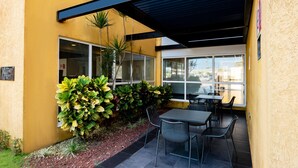 An outdoor patio area with tables and chairs, surrounded by yellow walls and large windows.
