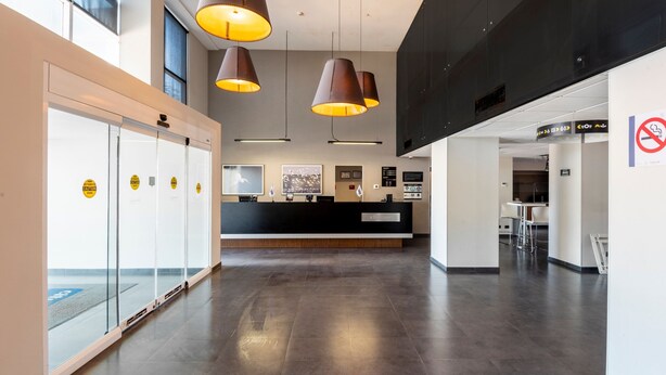 A modern hotel lobby with a reception desk, glass doors, and pendant lighting.