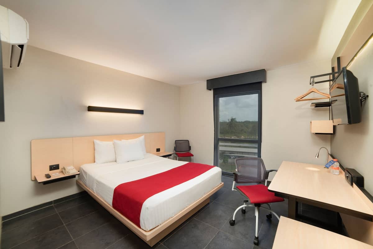 A hotel room with a bed, desk, chair, and a TV.