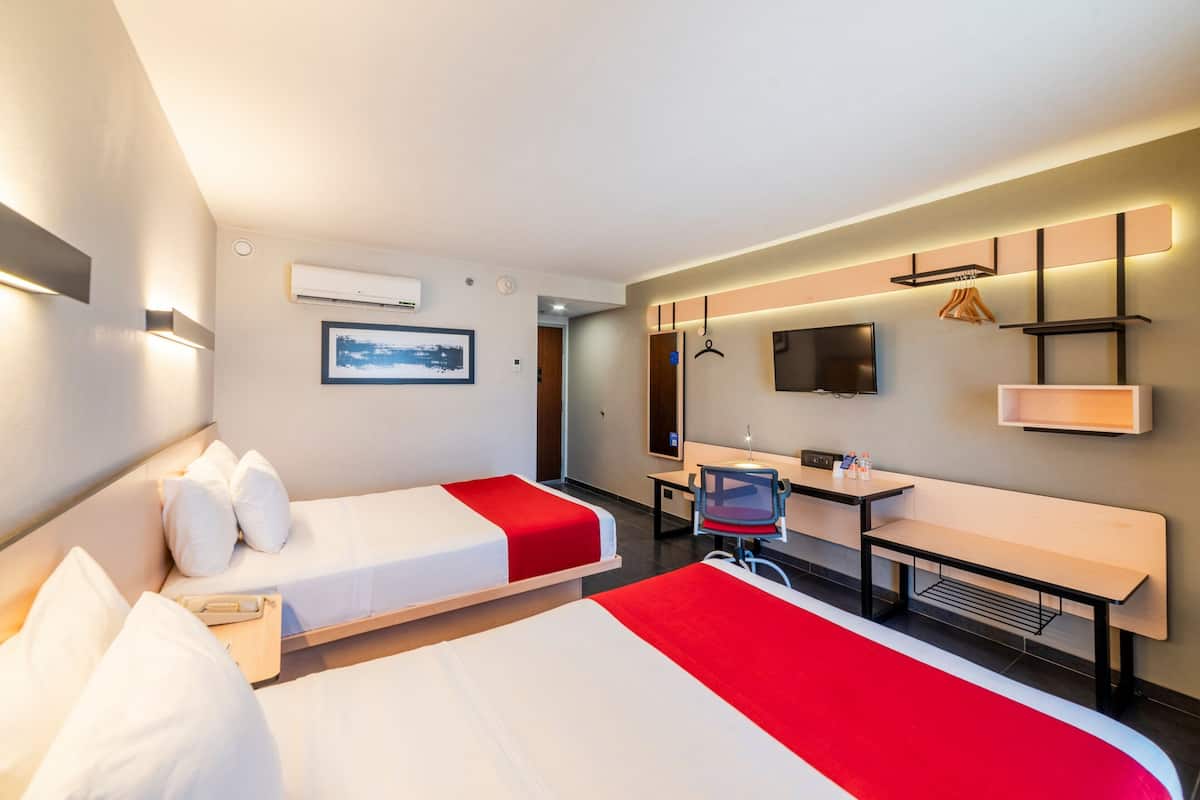 A hotel room with two beds, a desk, a chair, a TV, and a small seating area.