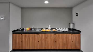 A kitchenette with a black countertop, wooden cabinets, and various food items.