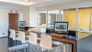 A reception area with two computer stations, a printer, and a phone. There are four white chairs and a wooden desk.
