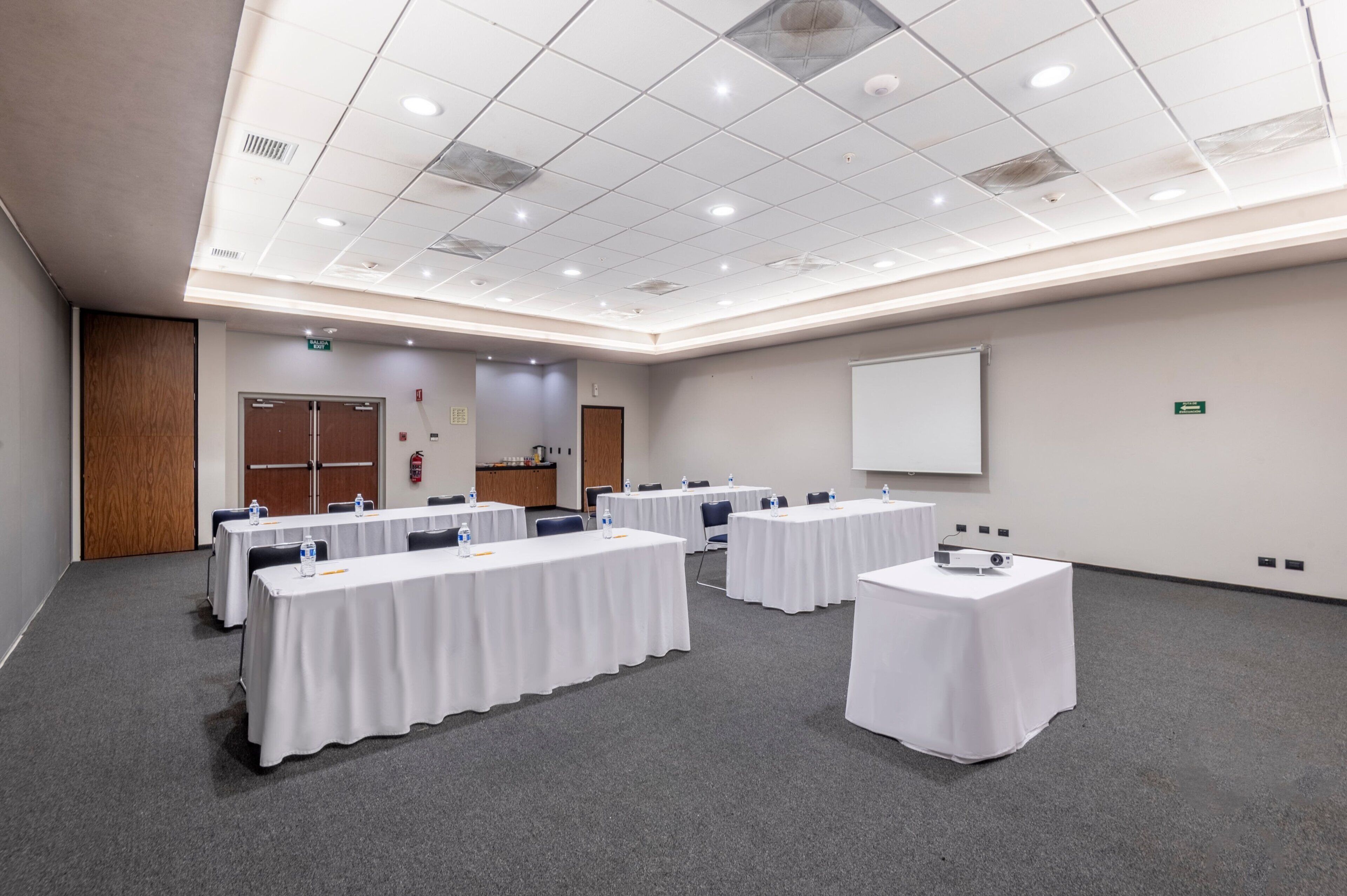 Une salle de conférence équipée de plusieurs tables, de chaises et d’un écran de projection.