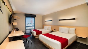 A hotel room with two beds, a desk, a chair, and a window with a view of a cityscape.