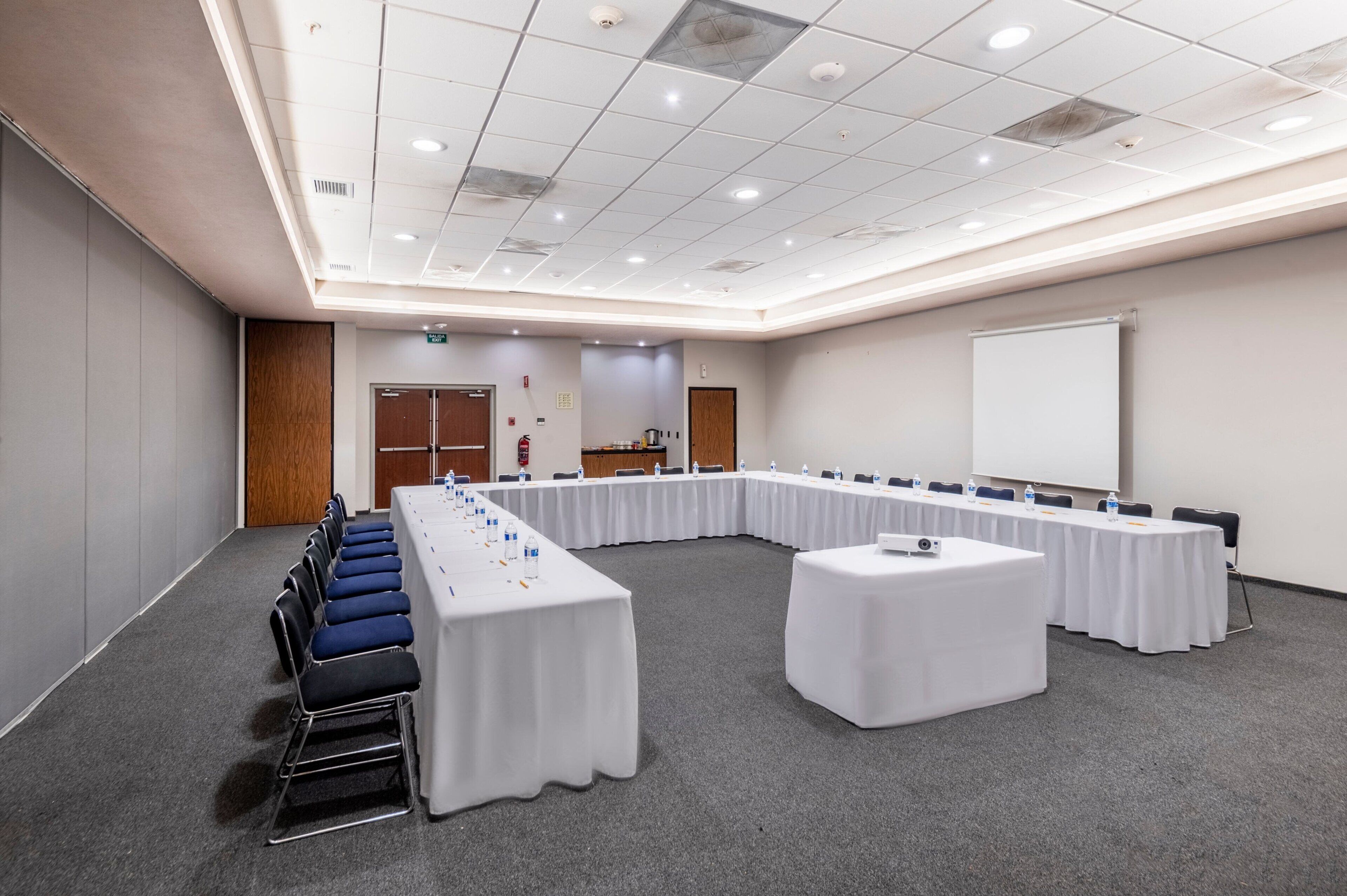 A conference room with a long table, chairs, and a projector screen.