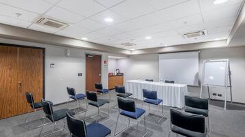 Une salle de conférence équipée d’un tableau blanc, d’un écran de projection et d’une table avec des chaises.