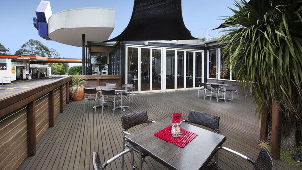 An outdoor dining area with tables and chairs, a large planter, and a view of a building with a unique architectural feature. - Nightcap at Morwell Hotel (Morwell)