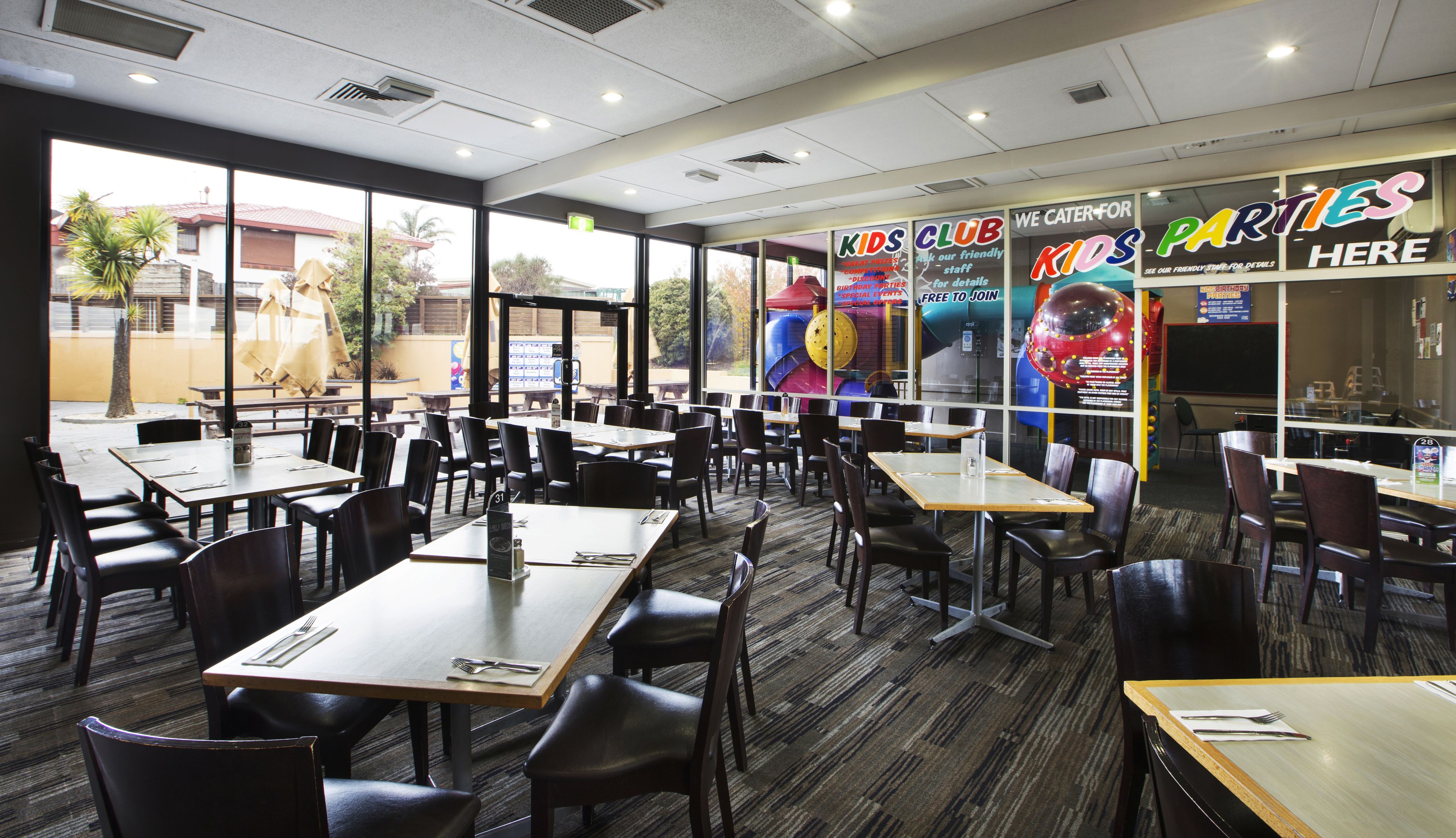 A restaurant with multiple tables and chairs, large windows, and colorful party decorations.