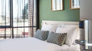 A hotel room with a large bed, two patterned pillows, a white headboard, and a view through a window with sheer curtains. - Nightcap at Morwell Hotel (Morwell)