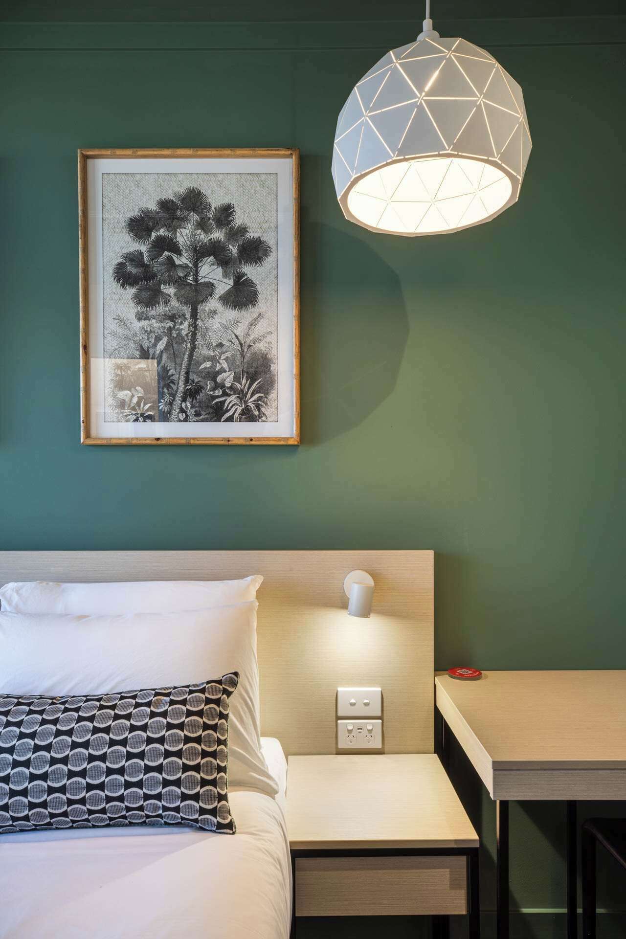 A neatly arranged hotel room with a bed, bedside table, and a wall-mounted lamp.