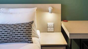 A neatly arranged hotel room with a bed, bedside table, and a wall-mounted lamp.