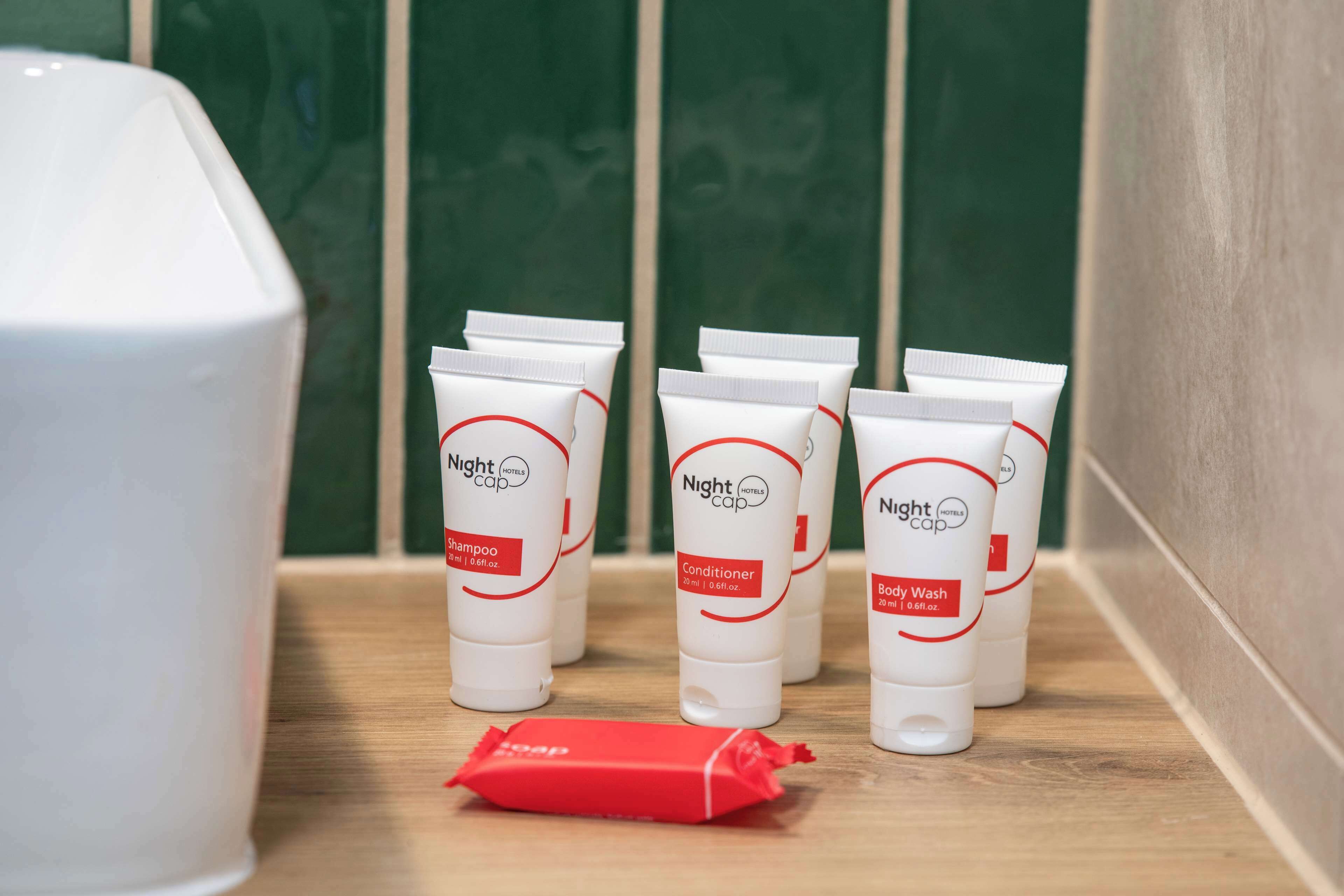 A row of toiletries on a shelf, including shampoo, conditioner, and body wash, with a red soap bar in front.