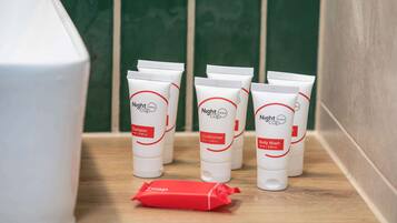 A row of toiletries on a shelf, including shampoo, conditioner, and body wash, with a red soap bar in front.