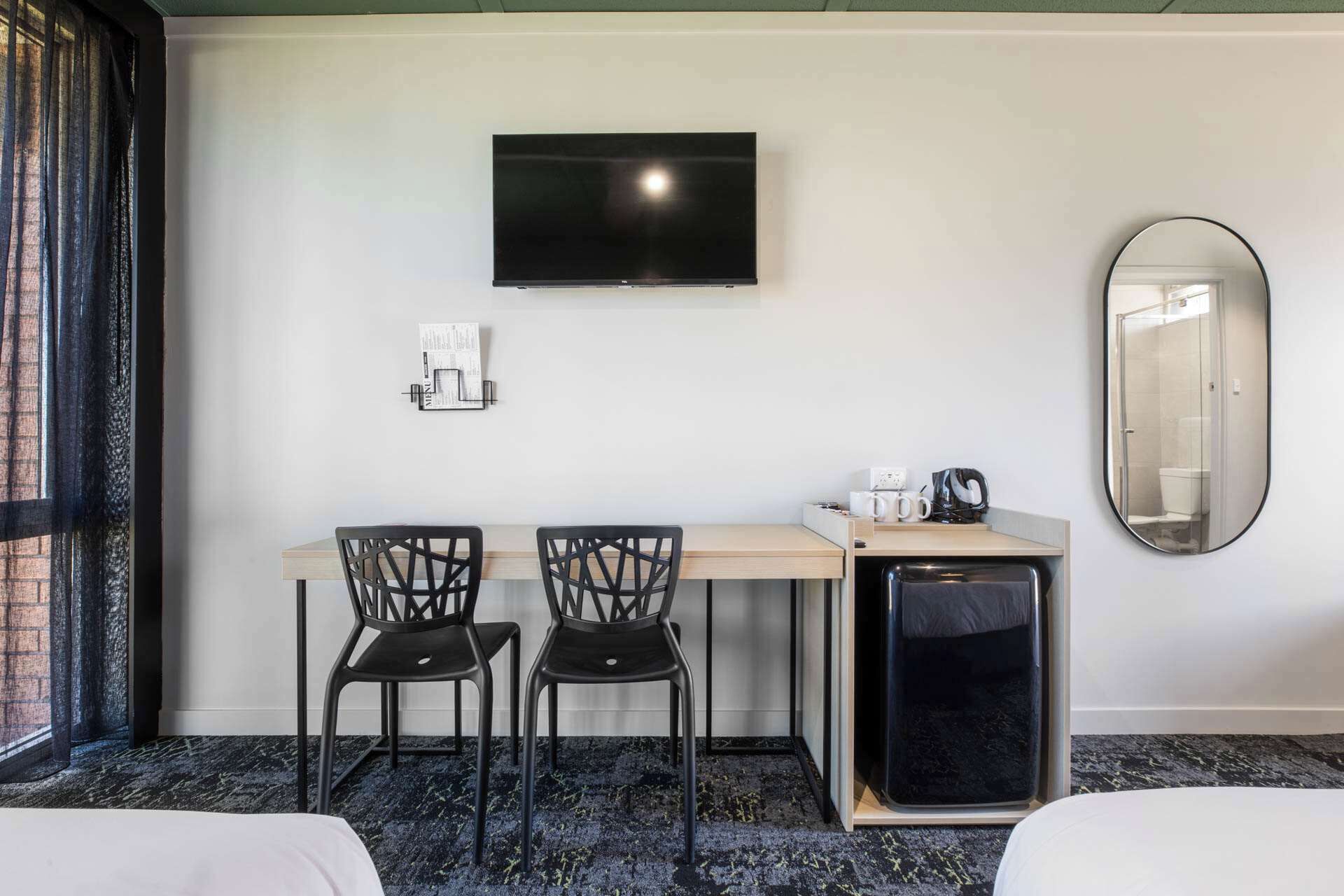A hotel room with a bed, a desk with two chairs, a television, a coffee machine, and a small refrigerator.