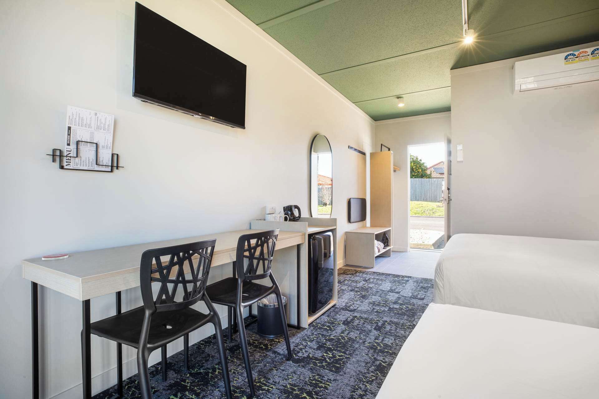 Une chambre d’hôtel comprenant un lit, un bureau avec deux chaises, un téléviseur à écran plat, un miroir et une porte donnant sur un balcon.