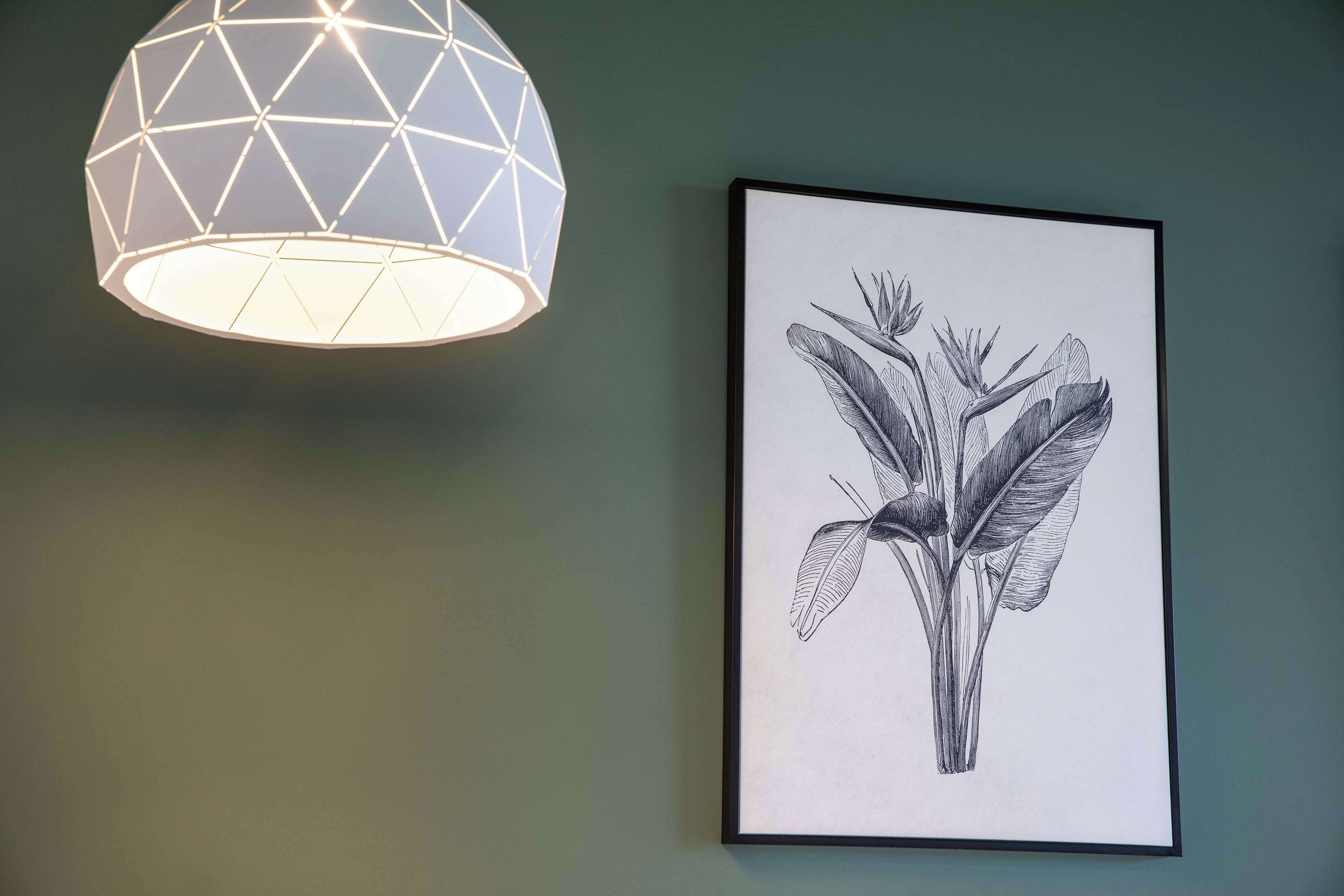 A geometric light fixture and a framed botanical illustration on a wall.