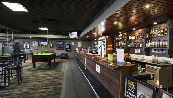 Zona de bar con mesa de billar, taburetes y una variedad de botellas de licores.
