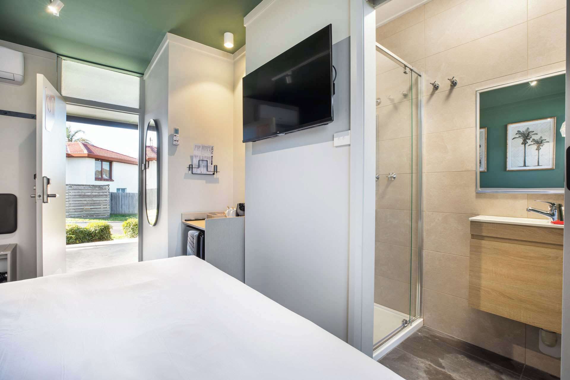 Ett modernt hotellrum med en säng, en TV som är monterad på väggen, en dusch och ett badrum med handfat och spegel.