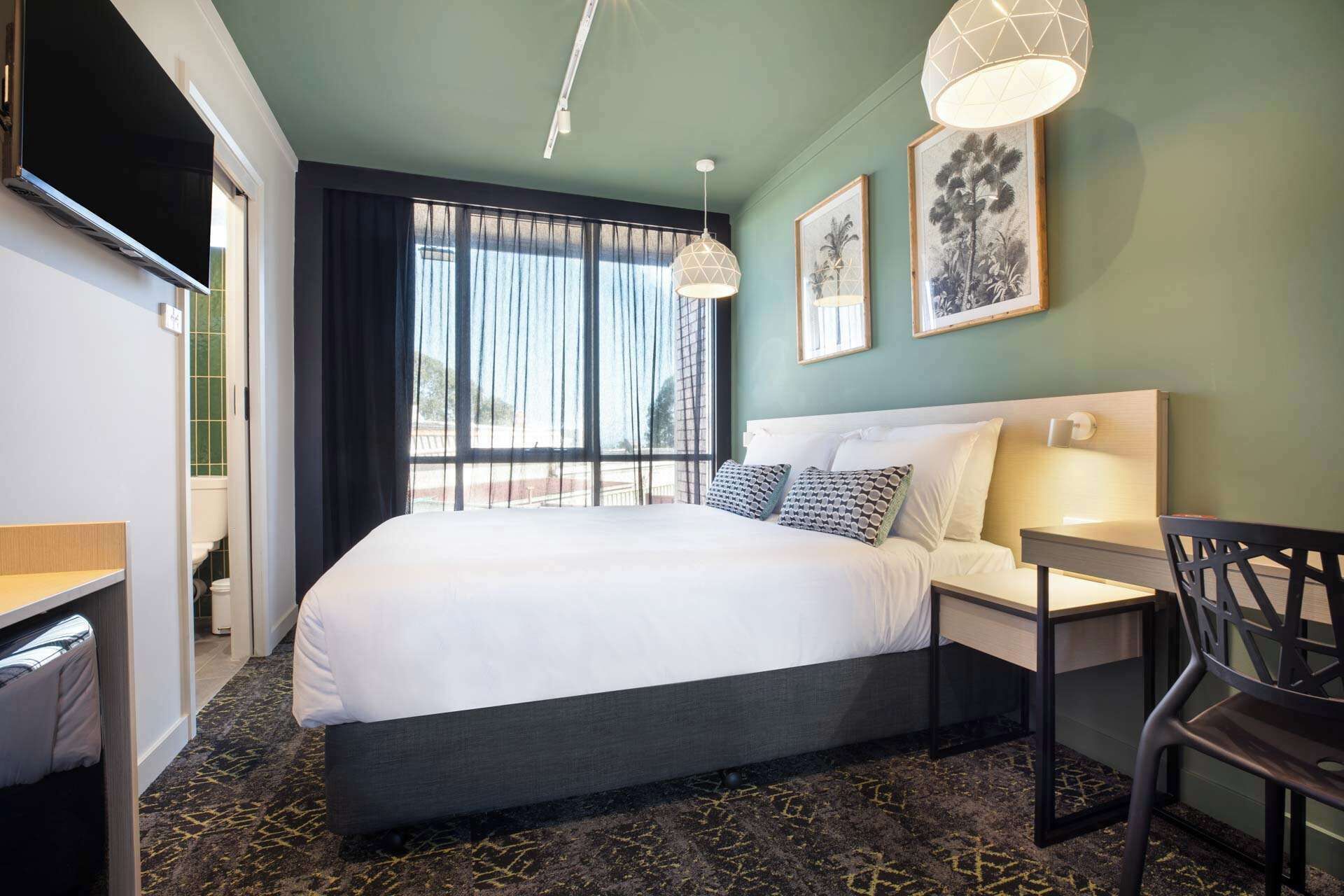 Ein Hotelzimmer mit Bett, Nachttisch, Stuhl und Schreibtisch.