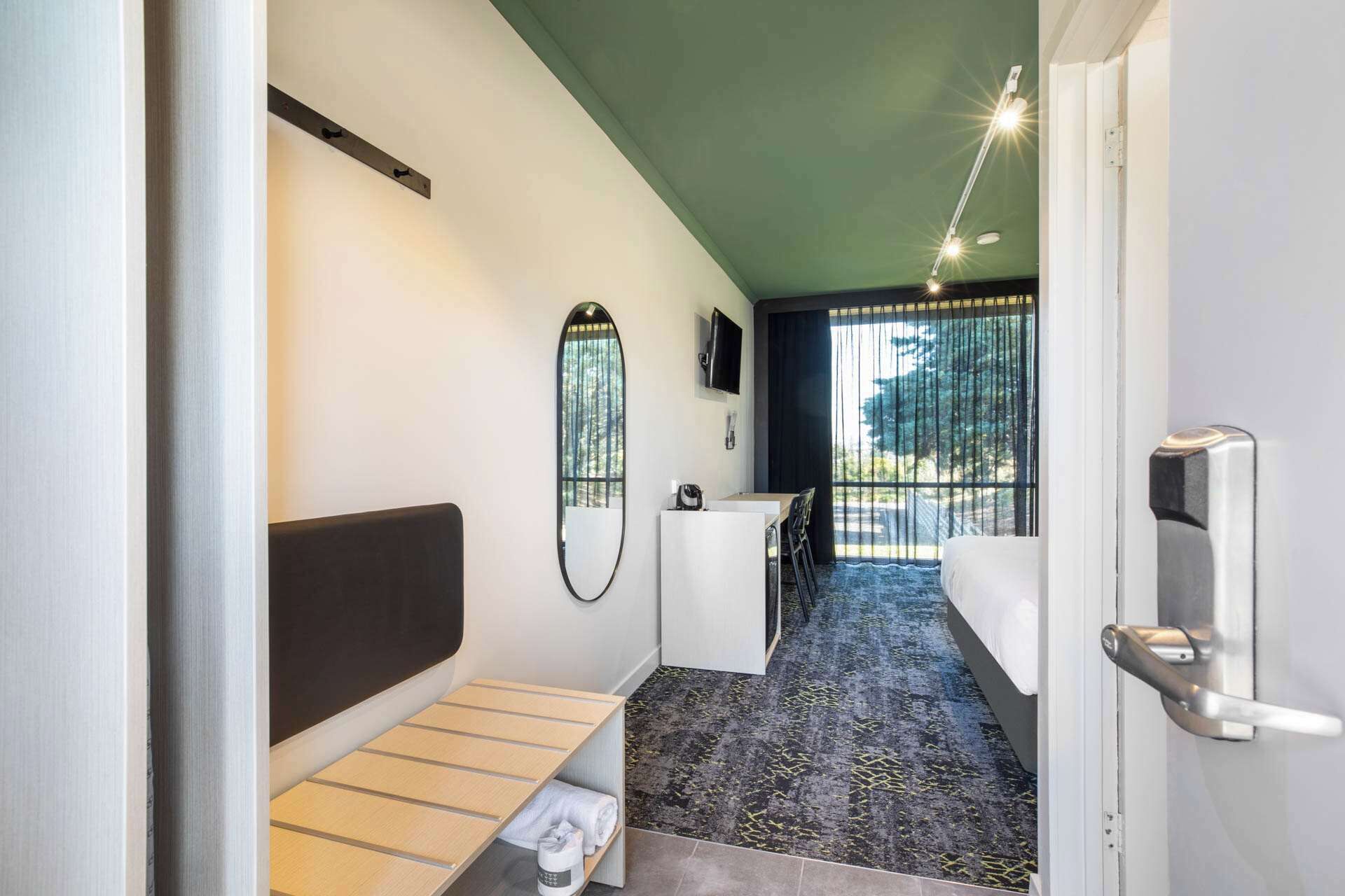 A narrow hallway with a bed, a desk, and a mirror.