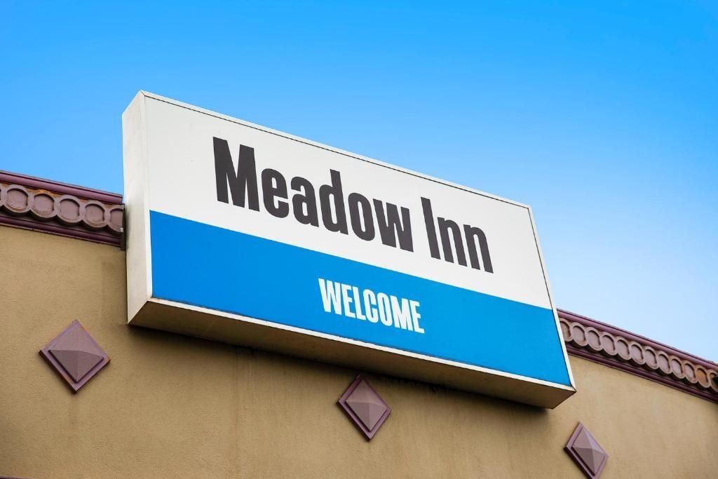 A sign for Meadow Inn with the words 'Meadow Inn' and 'WELCOME' on it.