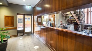 A reception area with a wooden reception desk, a plant, a fire extinguisher, and a staircase leading to an upper floor.