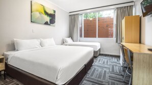 A hotel room with a large bed, two smaller beds, a desk, and a TV.