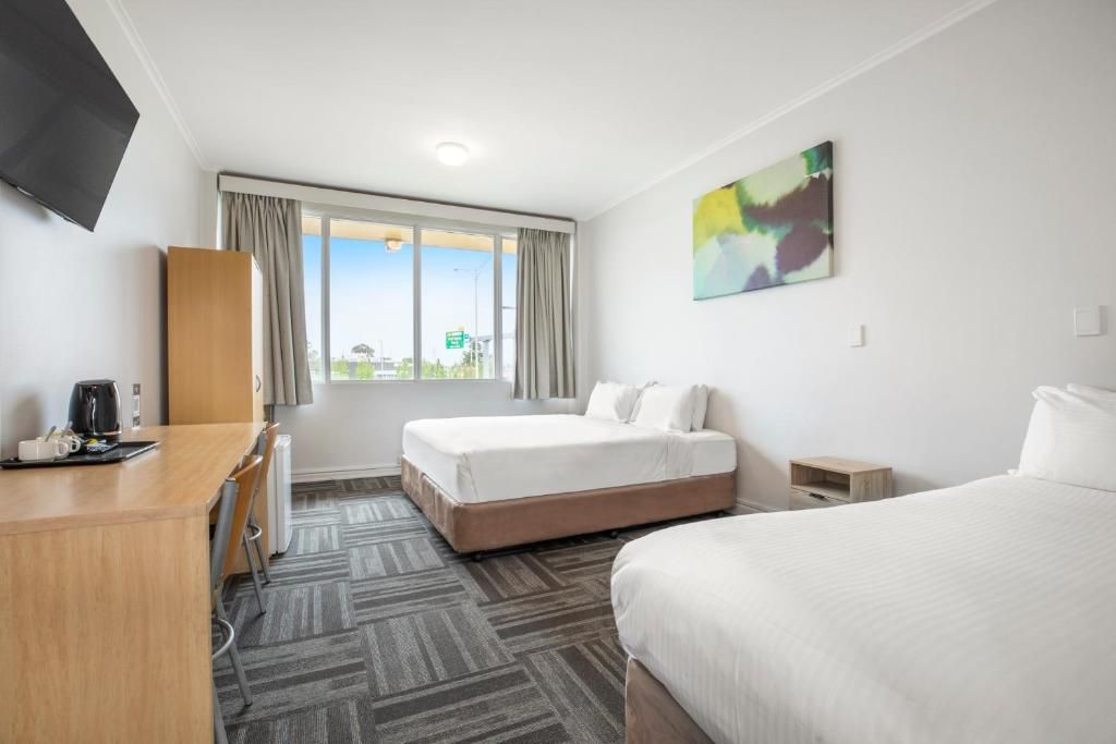 Ein Hotelzimmer mit zwei Betten, einem Schreibtisch, einem Stuhl, einem Fernseher und einem Fenster mit Vorhängen.