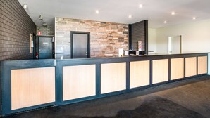 A reception area with a wooden reception desk, a stone accent wall, and a black door. - Nightcap at Westside Hotel (Laverton North)