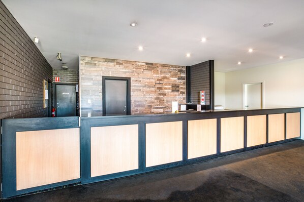 Zona de recepción con un mostrador de madera, un muro decorativo de piedra y una puerta negra.