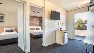 A hotel room with two beds, a small kitchenette, a flat-screen TV, and a door leading to a balcony.