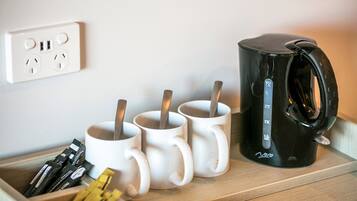 Un plateau en bois avec des tasses blanches, une machine à café noire et des sachets de thé ou de café.