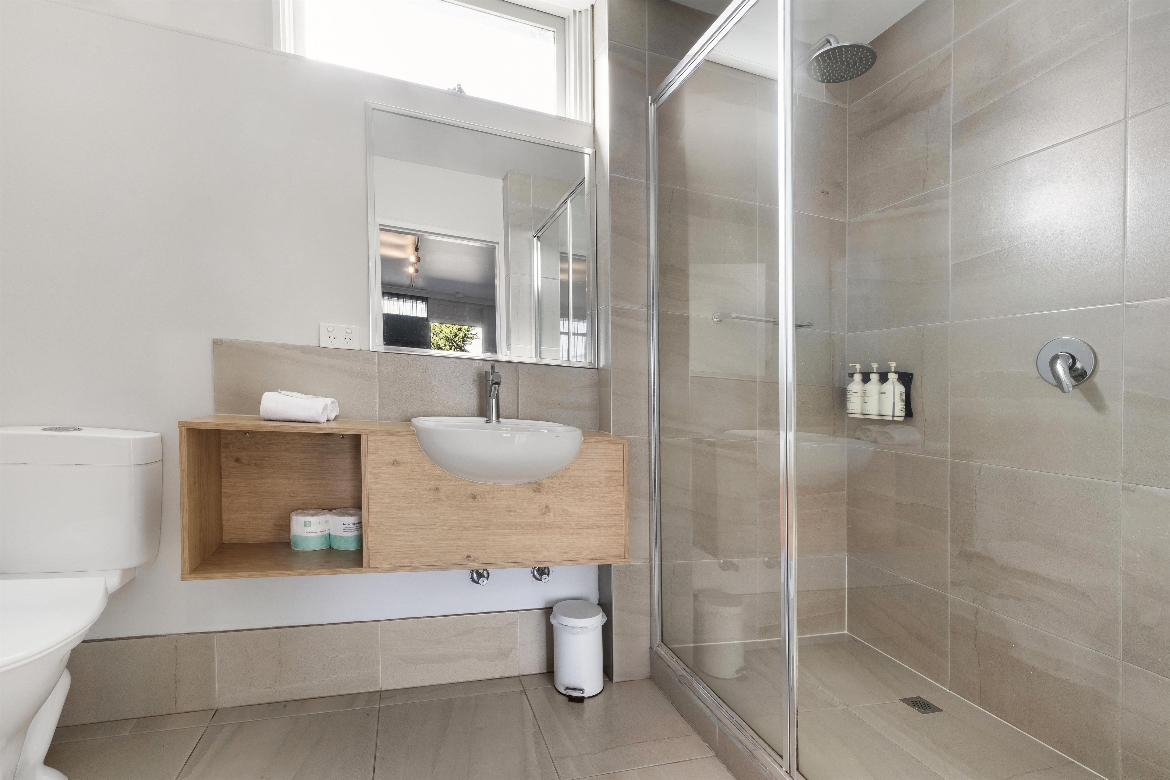 A modern bathroom with a glass-enclosed shower, a wooden vanity with a sink, and a toilet.