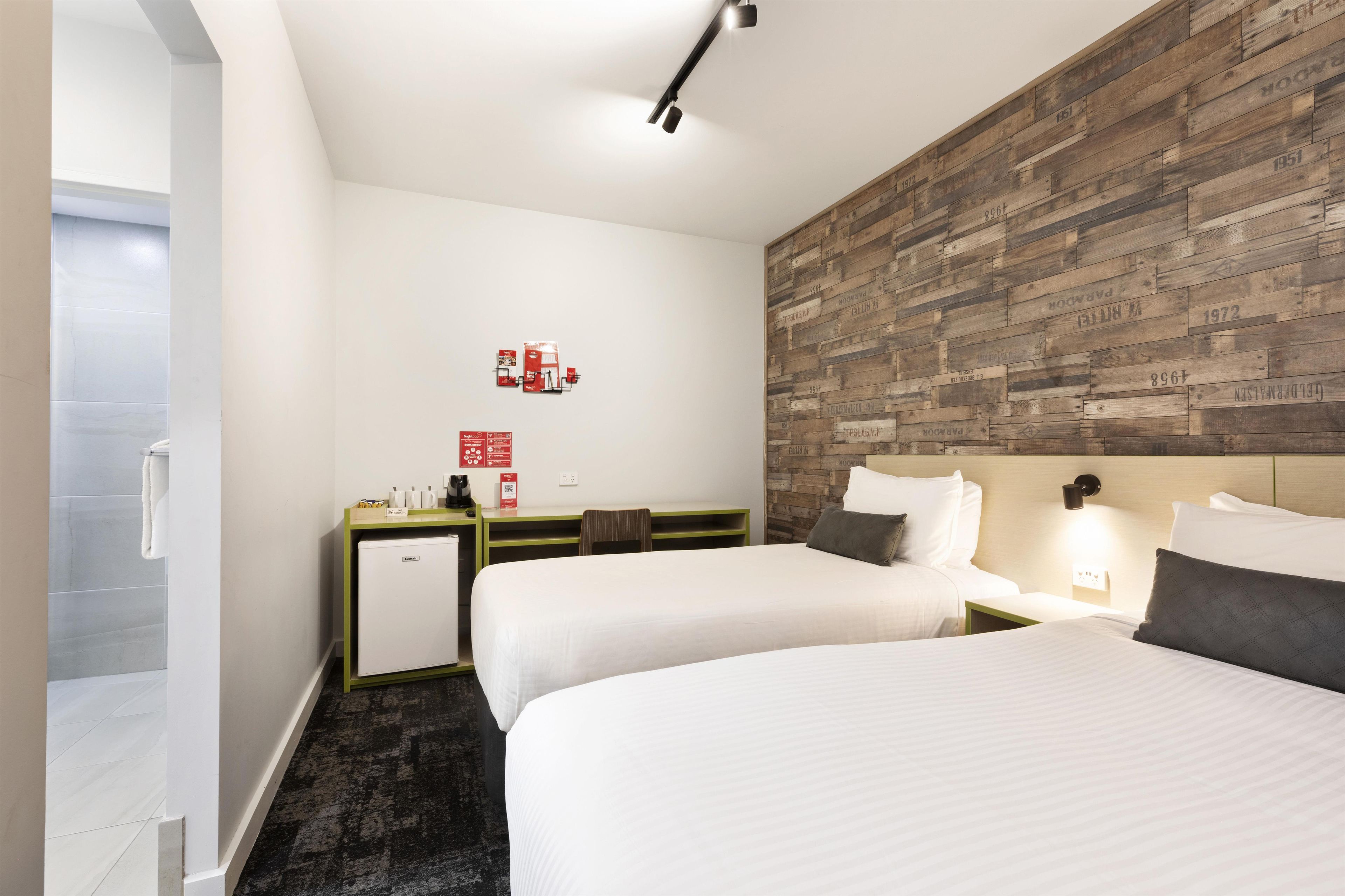 Une chambre d’hôtel avec deux lits, un petit bureau, un réfrigérateur et un mur décoratif en bois.