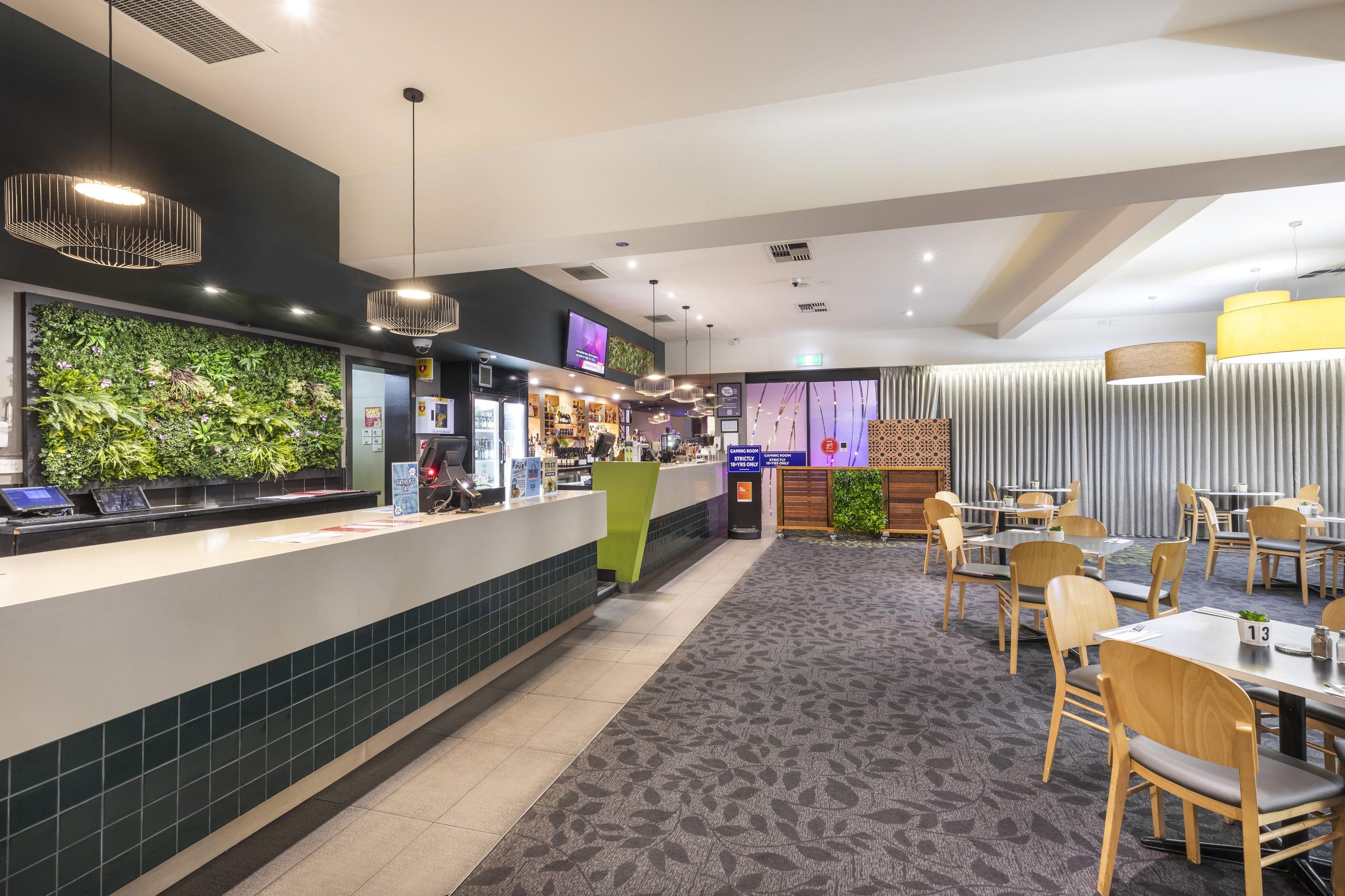 A restaurant with a counter, seating area, and a wall with greenery.