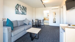 A modern living room with a grey sofa, a coffee table, and a dining area with chairs and a table. - Nightcap at Westside Hotel (Laverton North)