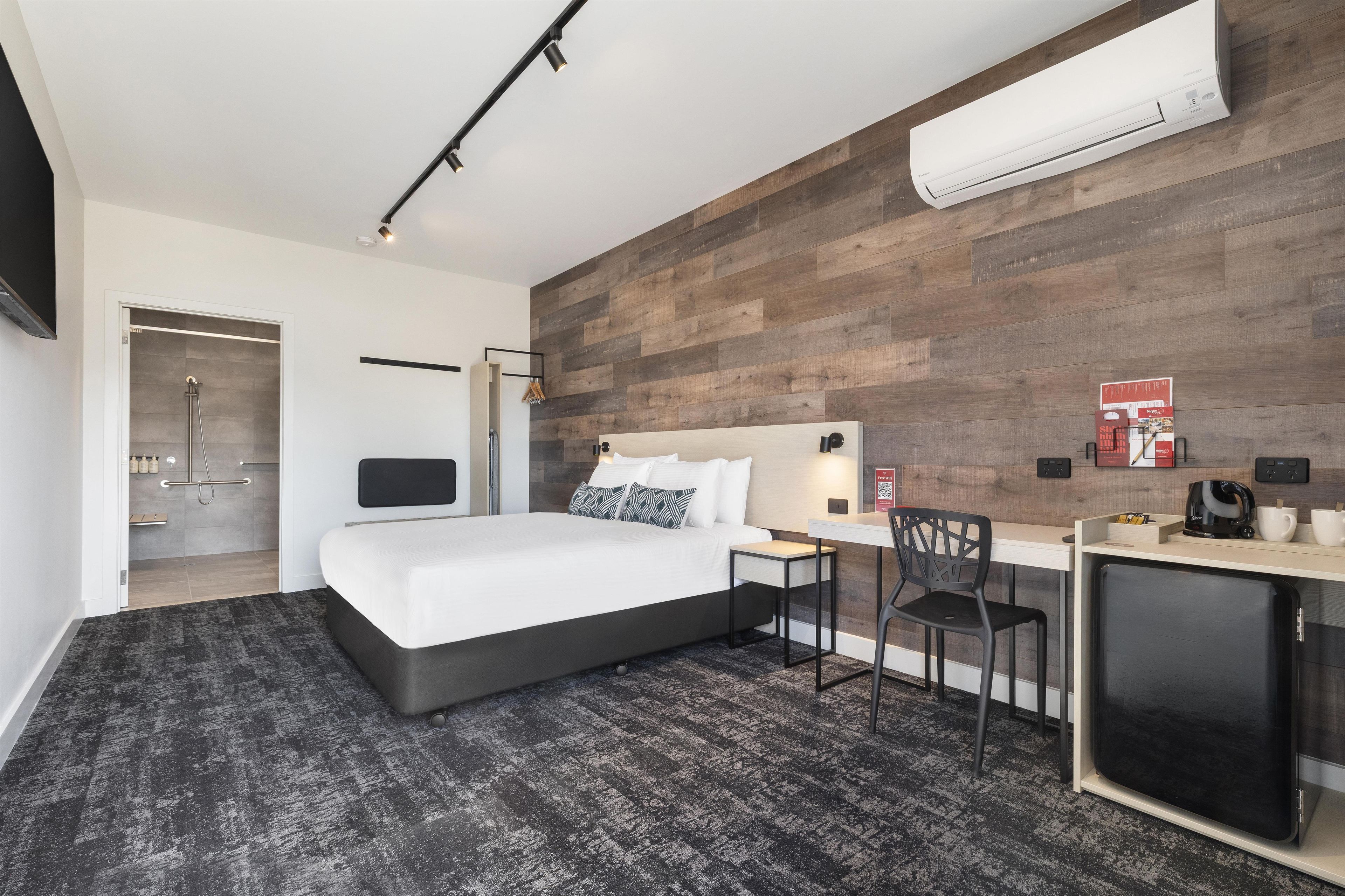 Una habitación de hotel moderna con cama, escritorio, silla y equipo de aire acondicionado.