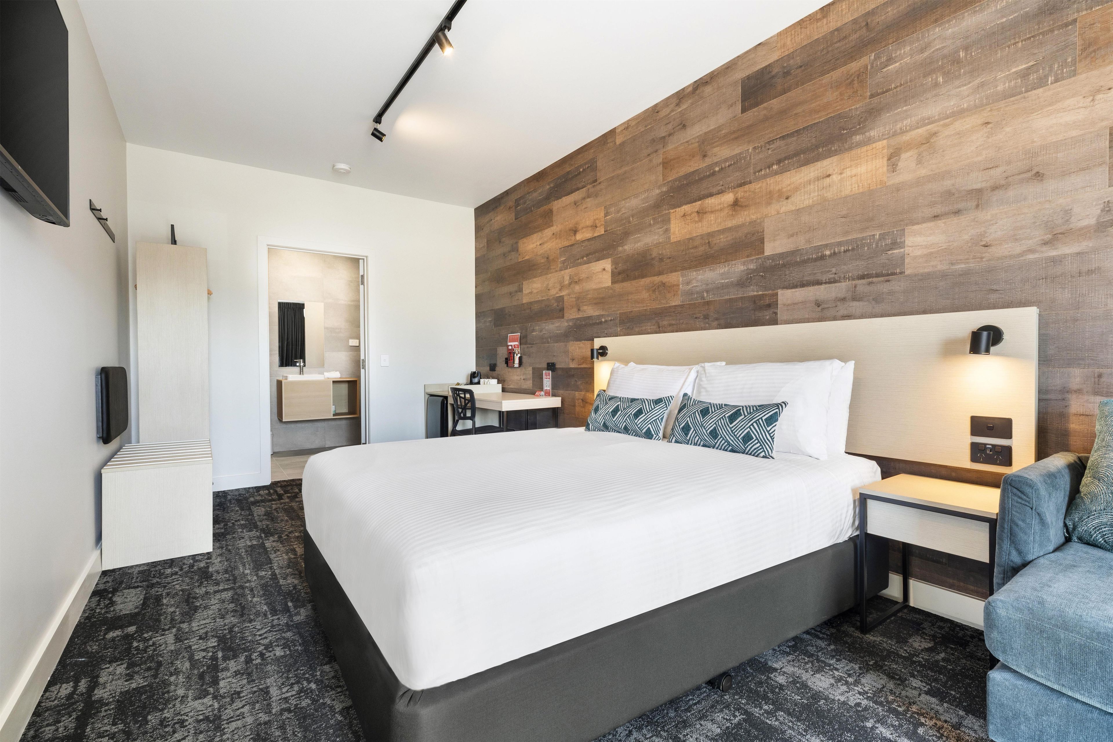 Habitación de hotel moderna con una cama grande, mesitas de noche, un escritorio y un televisor montado en la pared.