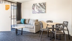 A modern room with a sofa, a small table, and a dining area with chairs. - Nightcap at Westside Hotel (Laverton North)