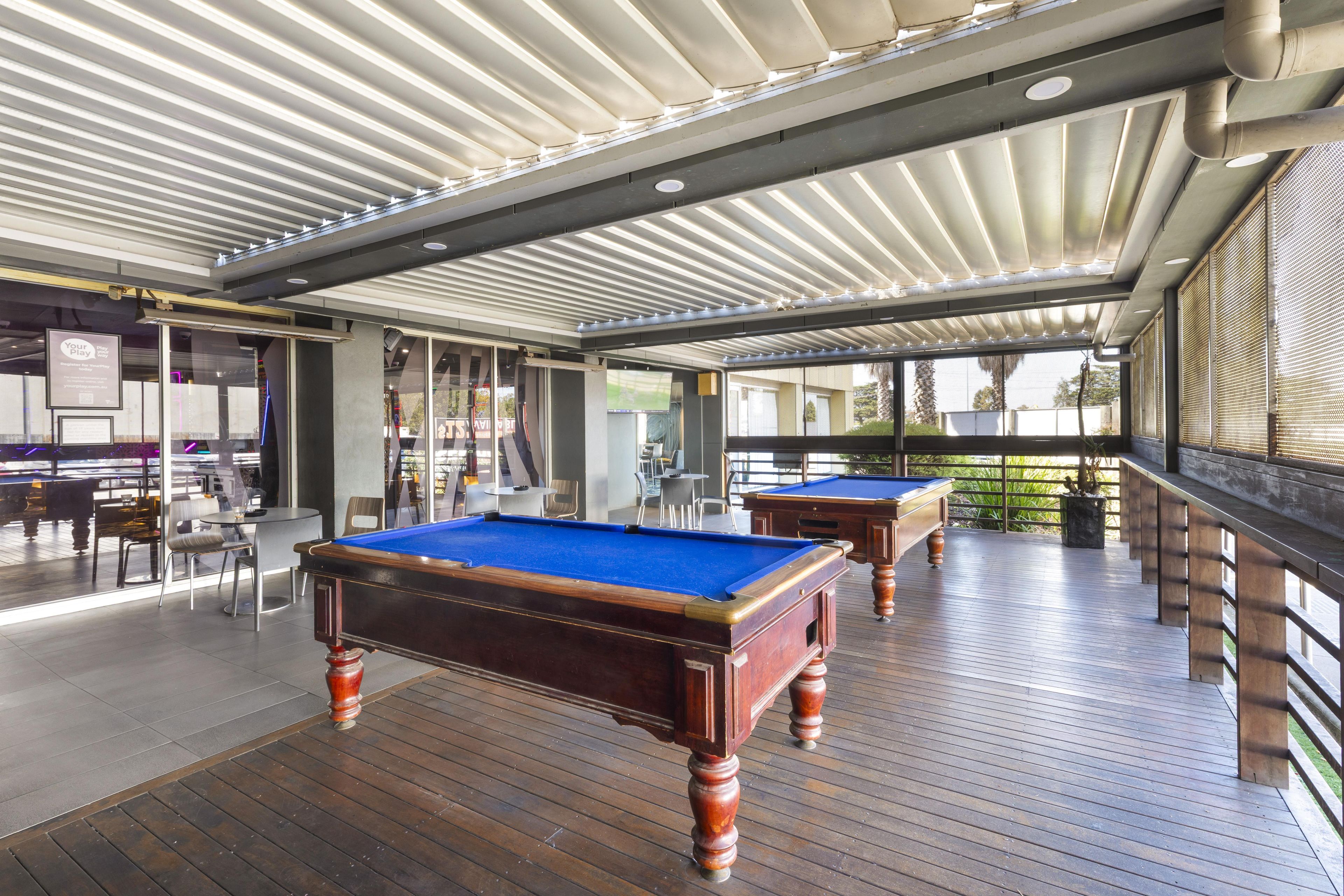Un espace dédié aux tables de billard, avec un plancher en bois, un plafond doté de luminaires linéaires et une vue sur l’extérieur grâce à de grandes fenêtres.
