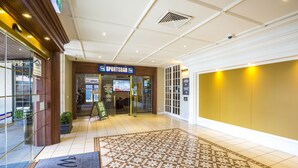 Un vestíbulo de hotel con un tapete de bienvenida, un bar deportivo y un cartel que indica 'Todas las habitaciones disponibles'.