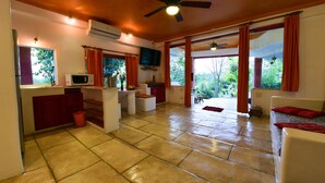 A spacious living area with a kitchen, a ceiling fan, and large windows with curtains. - Mirabel Resort & Mini Golf (Pattaya)
